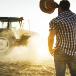 Ein junger Bauer blickt gegen die Sonne in Richtung seines Traktors