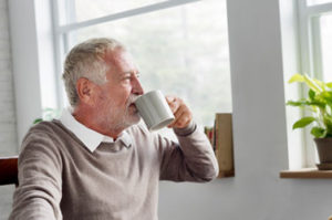 Ein älterer Herr sitzt am Fenster, schaut hinaus und trinkt einen Kaffee