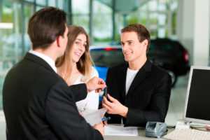 Ein glückliches junges Paar erhält einen Autschlüssel vom Autohändler
