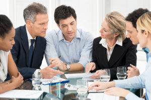 Mehrere Personen im Business Outfit besprechen sich an einem großen Glastisch