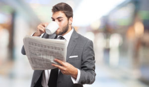 Junger Mann mit Anzug trinkt eine Tassee Kaffee und liest die neueste Zeitung