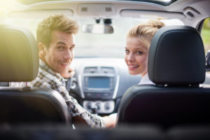 Ein junges Paar sitzt vorn im Auto und dreht sich lächelnd nach hinten um