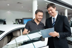 Ein Autohändler steht mit seinem Kunden neben einem Auto und erklärt ihm Vertragdetails