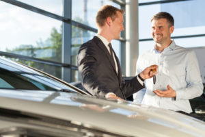 Ein Autohändler übergibt seinem Kunden einen Autoschlüssel