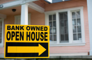 Vor einem rosa farbenen Haus steht ein Schild, das auf den Verkauf durch die Bank hinweist