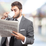 Junger Mann im Anzug trinkt Kaffee und ließt Zeitung