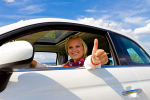 Eine junge lächelnde Frau zeigt den erhobenen Daumen aus dem Autofenster