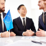 Drei Männer im Anzug im Hintergrund vor europäischer Fahne auf Tisch
