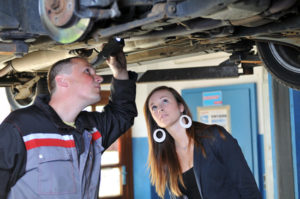 Ein Mechaniker und eine junge Frau inspezieren ein Auto von unten