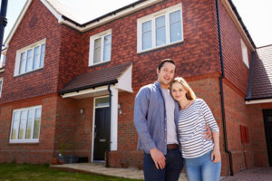 Ein glückliches junges Paar steht vor einem schönen Haus aus roten Klinkersteinen