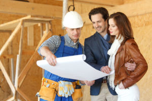 Glückliches Paar und Handwerker mit Bauplan auf der Baustelle für ein Holzhauses