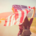 Eine gelöste junge Frau in der Natur lässt eine US-Flagge wehen