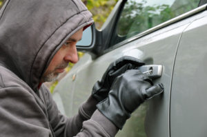 Ein Mann mit Kaputzenpulli und Handschuhen versucht ein Autoschluss zu knacken