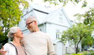 Ein lächelndes älteres Paar steht vor einem schönen weißen Haus