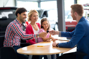 Eine lachende Familie nimmt beim Autohändler einen Autoschlüssel entgegen