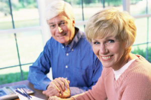 Ein älteres Paar sitzt lächelnd am Schreibtisch vor einem Taschenrechner