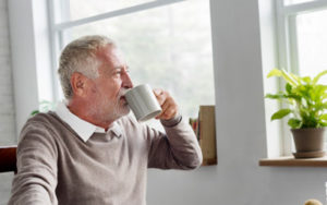 Ein älterer Mann trinkt Kaffee und sieht dabei aus dem Fenster