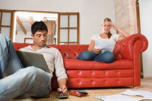 Ein junges Paar sitzt auf einer roten Couch und rechnet Unterlagen nach