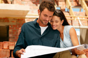 Glückliches Paar studiert einen Bauplan vor einem Haus im Rohbau