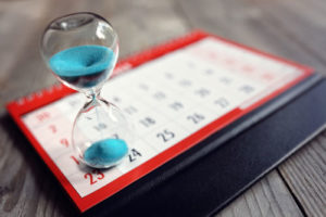 Eine Eieruhr mit blauem Sand steht auf einem Kalender
