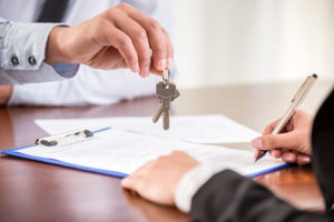 Ein Mann unterschreibt einen Vertrag während ein anderer ihm zwei Hausschlüssel reicht