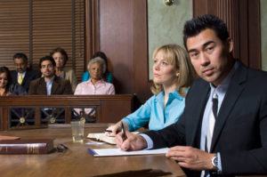 Ein Anwalt und eine Frau sitzen am Tisch vor einem Gericht und haben Unterlagen vor sich